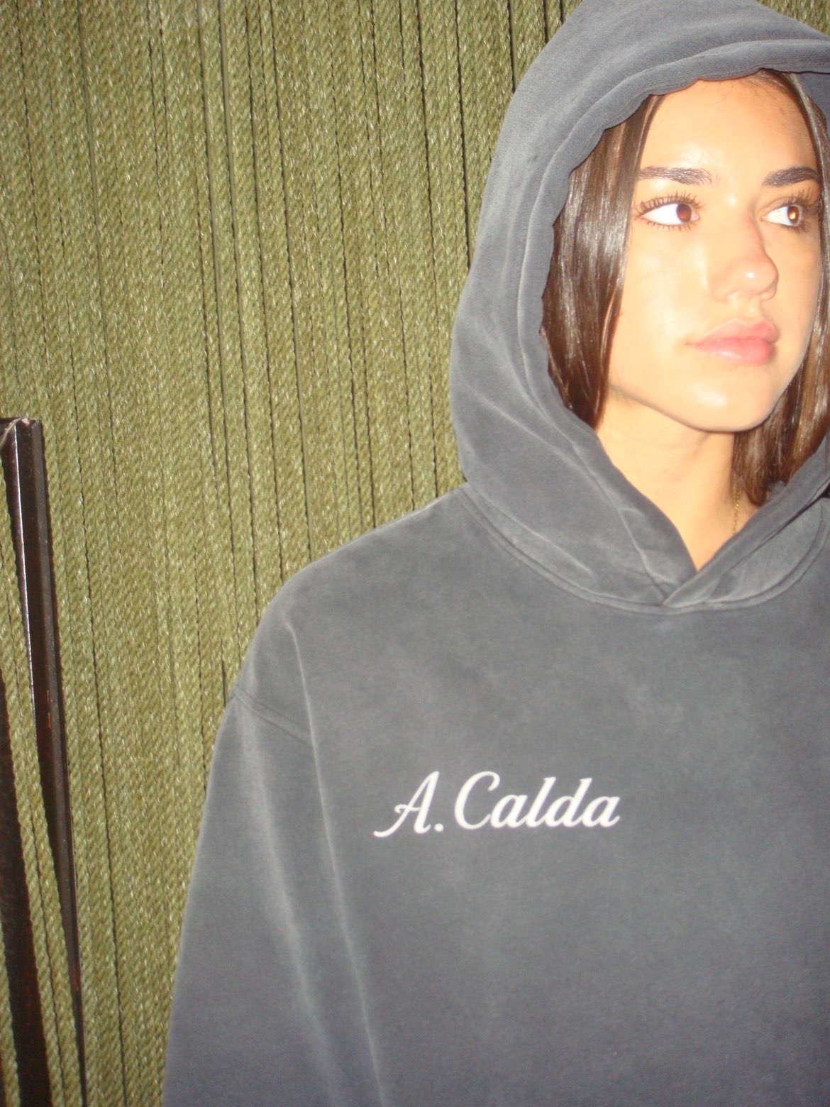 Val wearing the A. Calda hoodie against a green textured wall